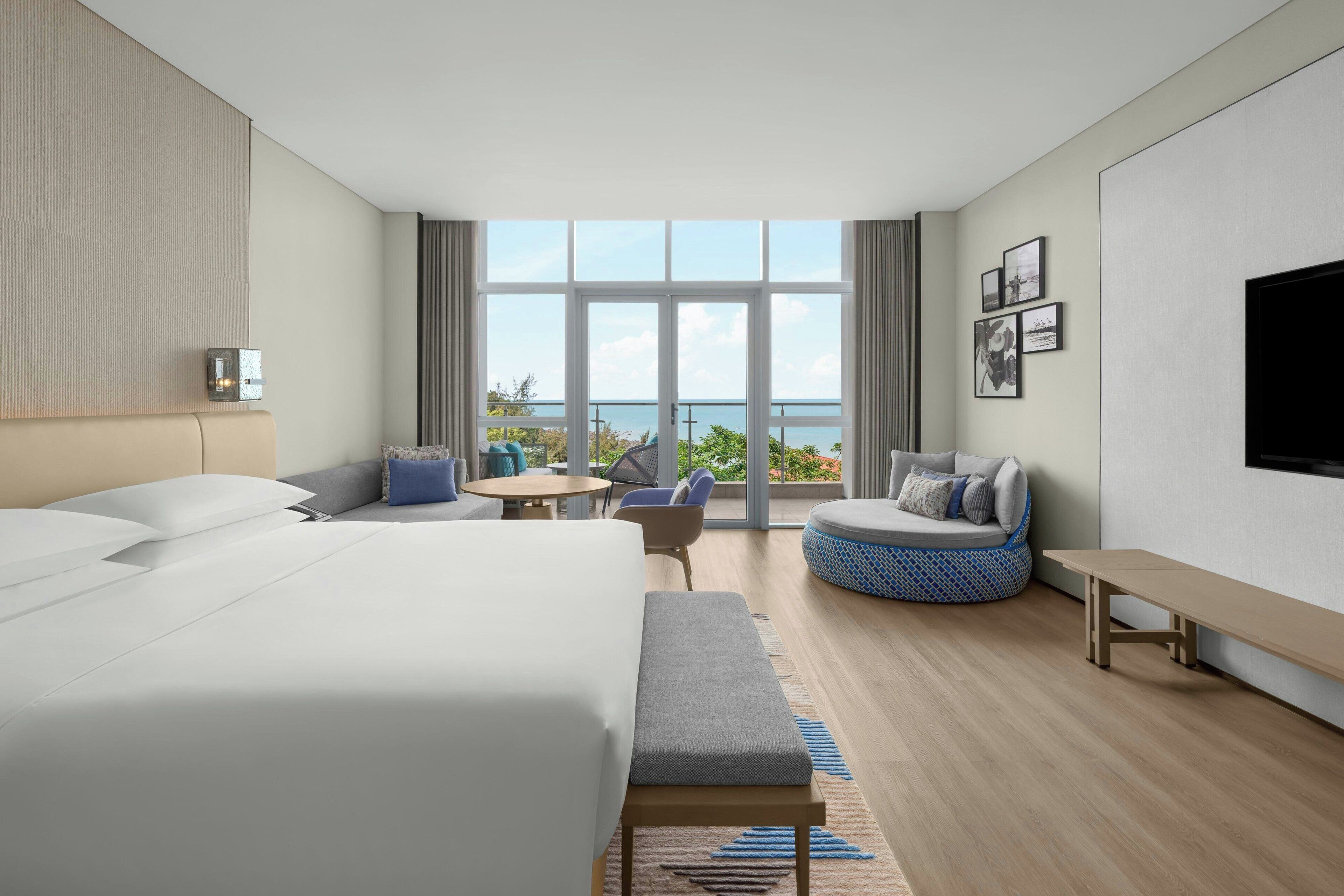 Una habitación de hotel moderna con una cama grande, una zona de estar con vistas y un televisor de pantalla plana.
