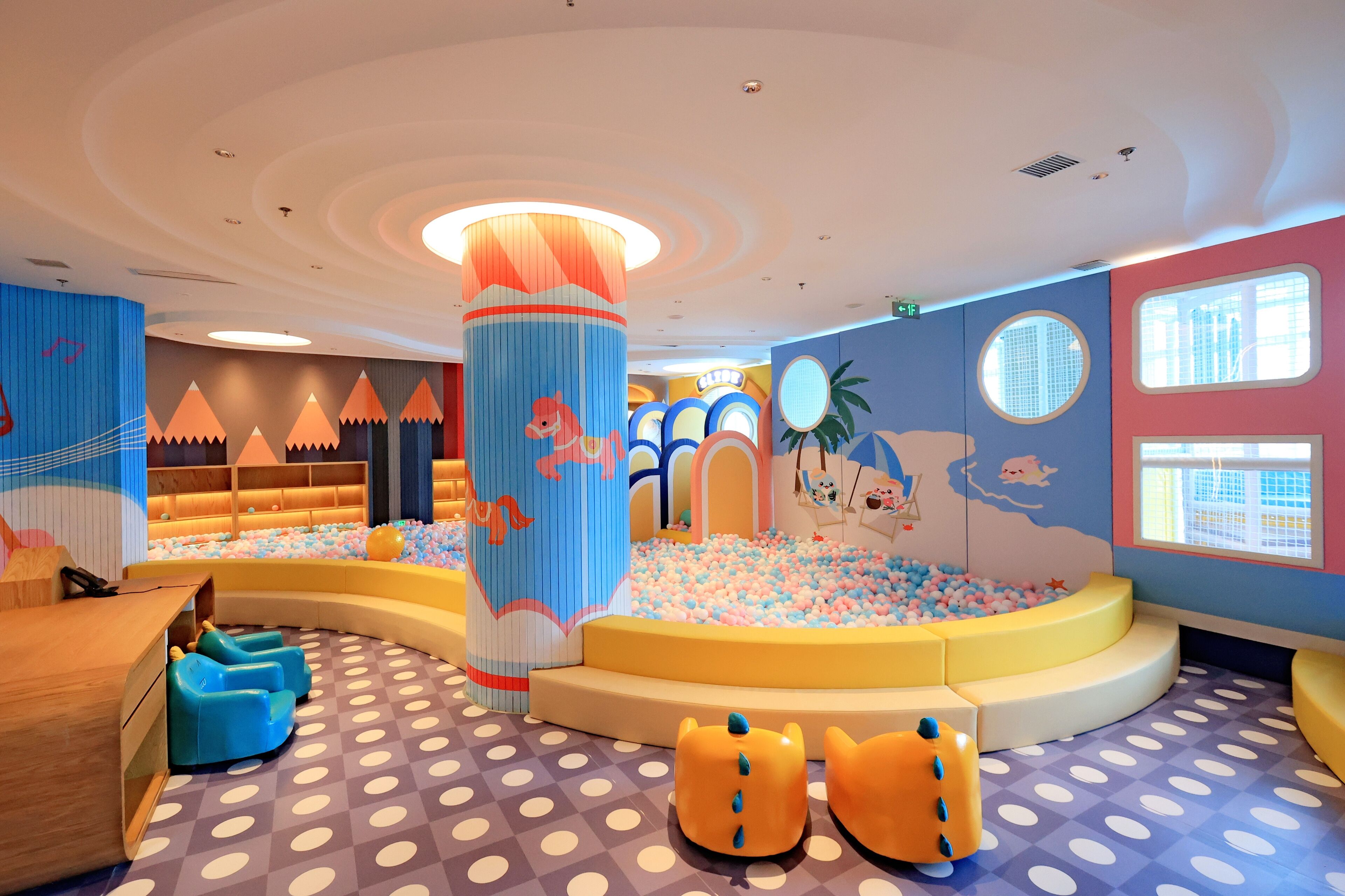 Zona de juegos infantiles con paredes coloridas, una piscina de pelotas y un pilar con un personaje de caricatura.