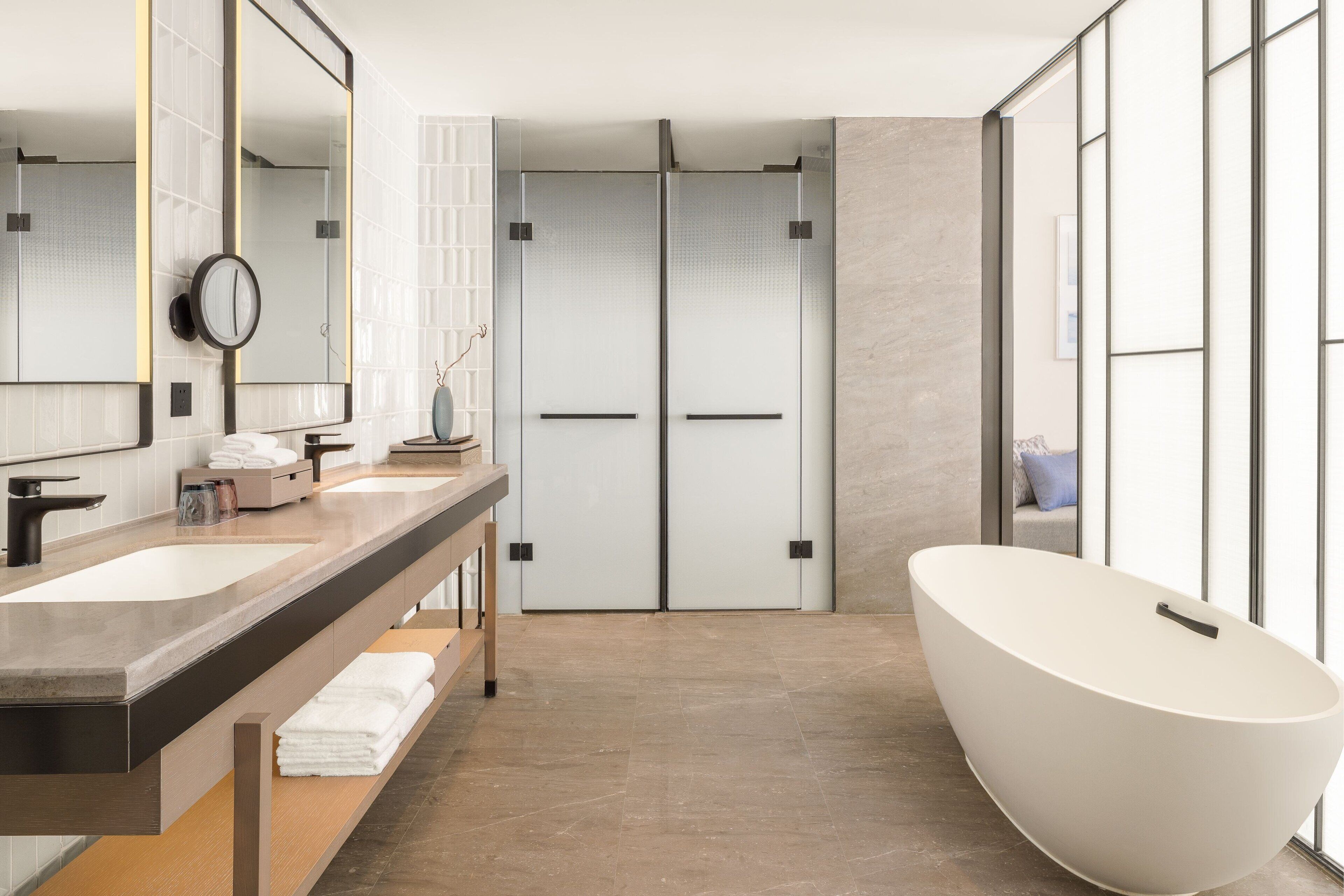 A modern bathroom with two sinks, a large mirror, a freestanding bathtub, and a glass shower enclosure.