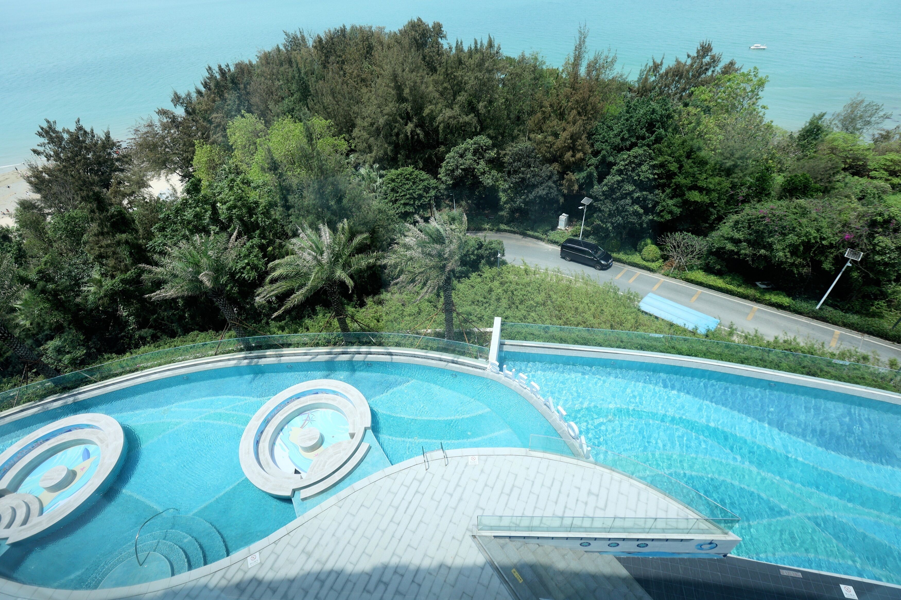 Una piscina con diseño circular, rodeada de abundante vegetación y una carretera.