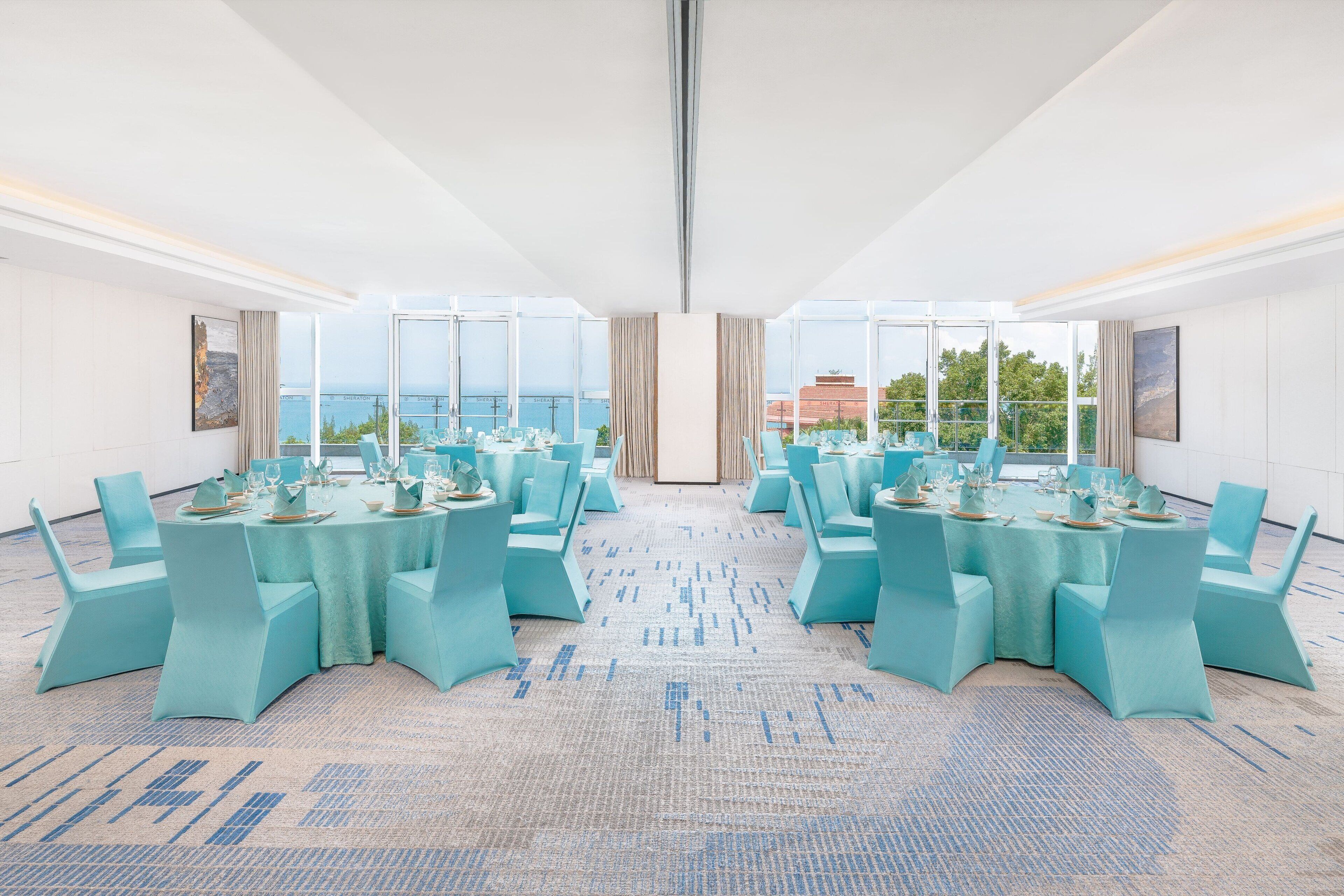 Een vergaderruimte met ronde tafels, teal stoelen en een vloerbedekking.