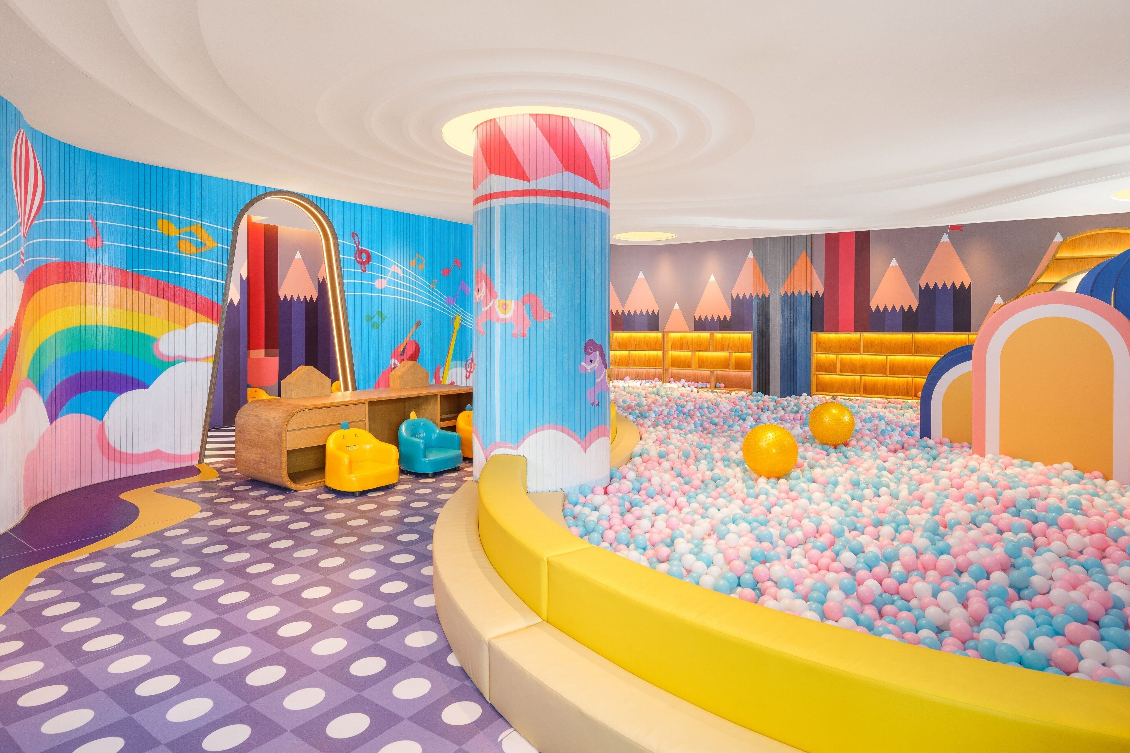 Un área de juegos llena de color, con un foso de pelotas, un espejo grande y un mural de arcoíris.