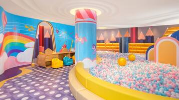 Un área de juegos llena de color, con un foso de pelotas, un espejo grande y un mural de arcoíris.