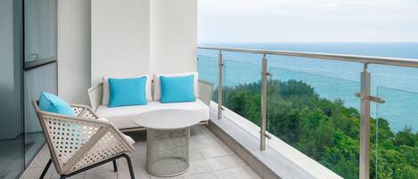 A balcony with a white sofa, two blue cushions, a wicker chair, and a small round table.