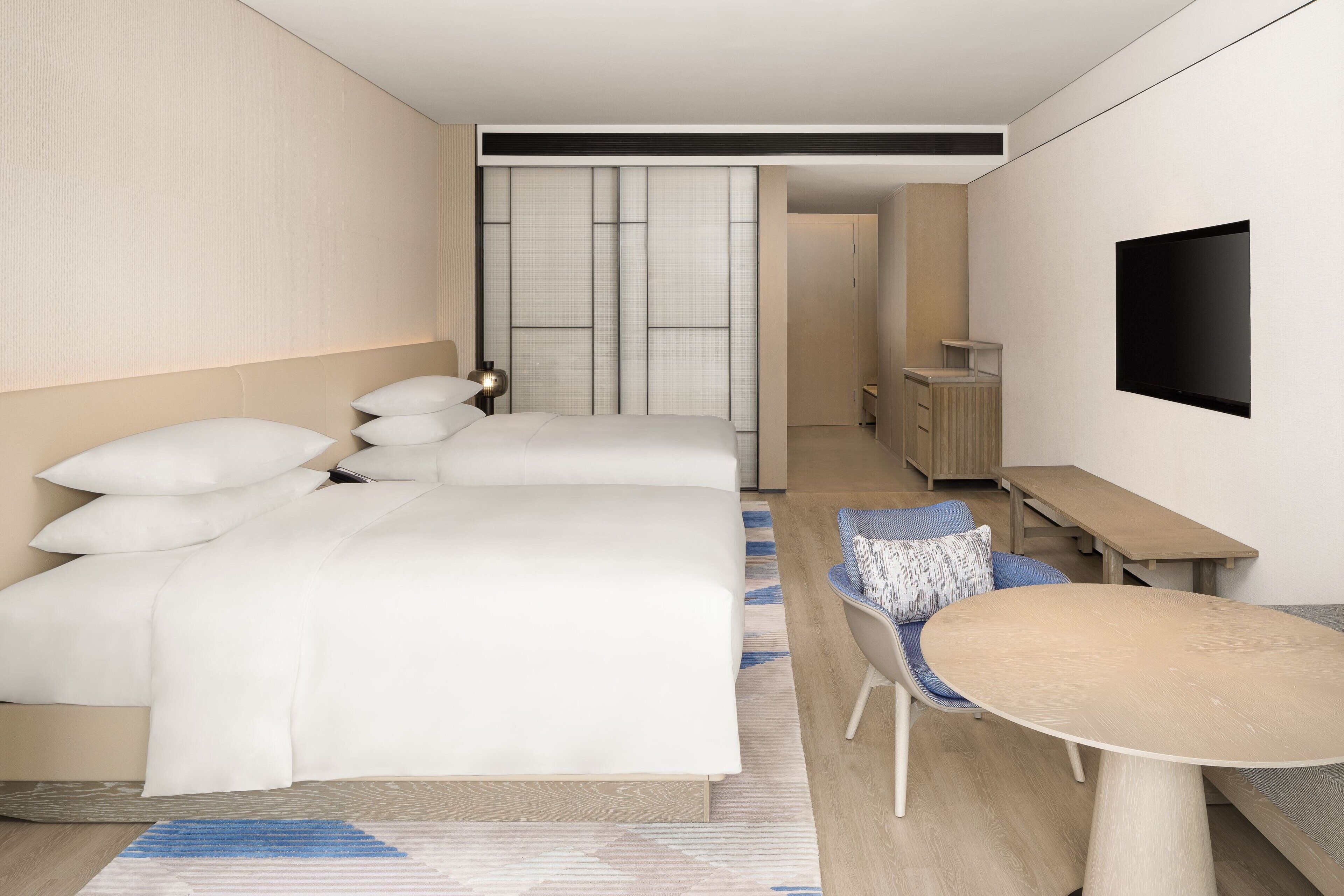Una habitación de hotel moderna con dos camas, un escritorio, una silla y un televisor.