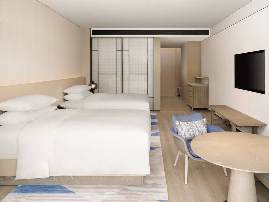 Una habitación de hotel moderna con dos camas, un escritorio, una silla y un televisor.
