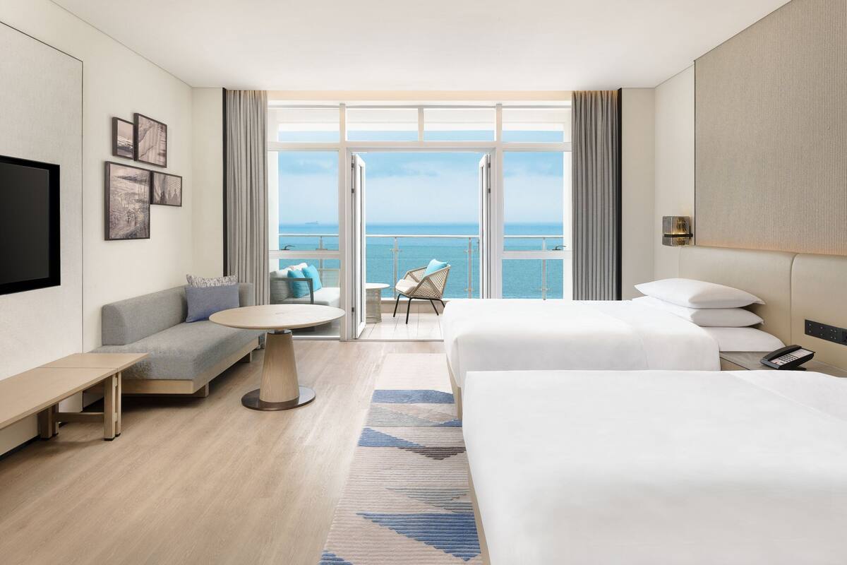 A modern hotel room with a balcony, a sofa, a bed, a desk, and a TV.