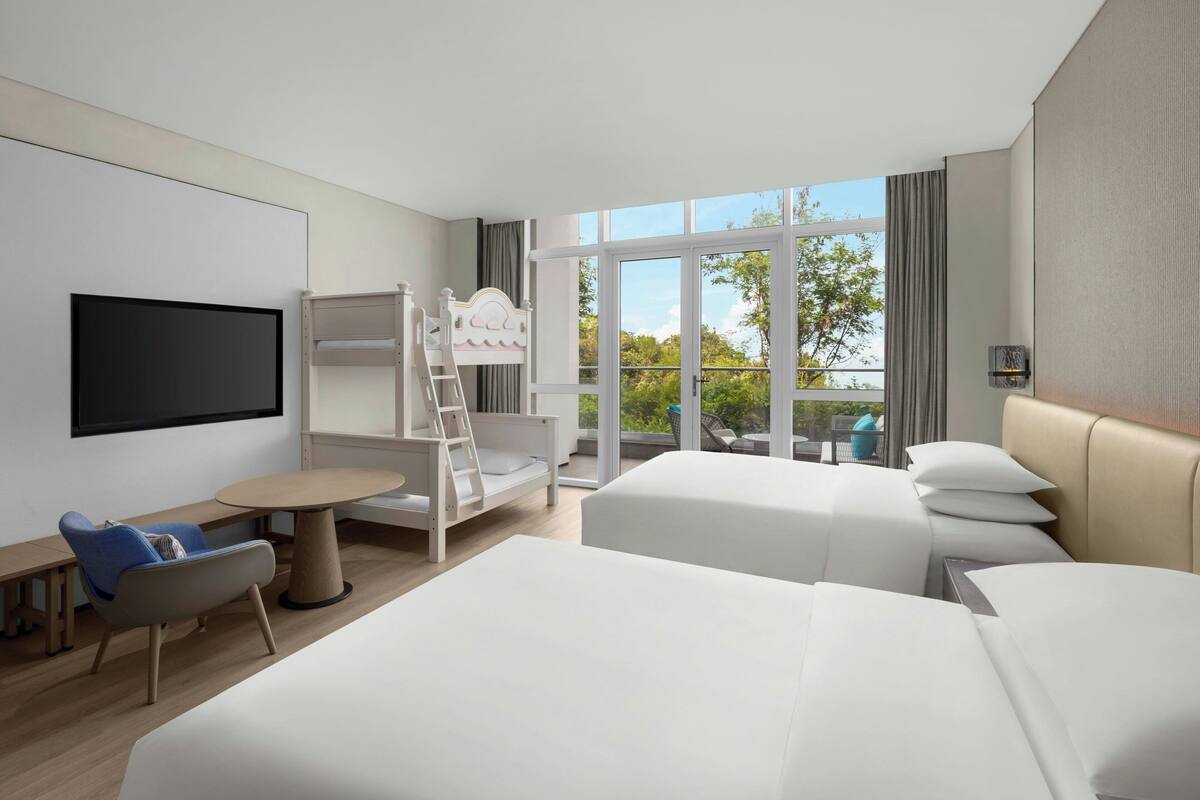 A hotel room with two beds, a TV, a desk, and a balcony with a view.