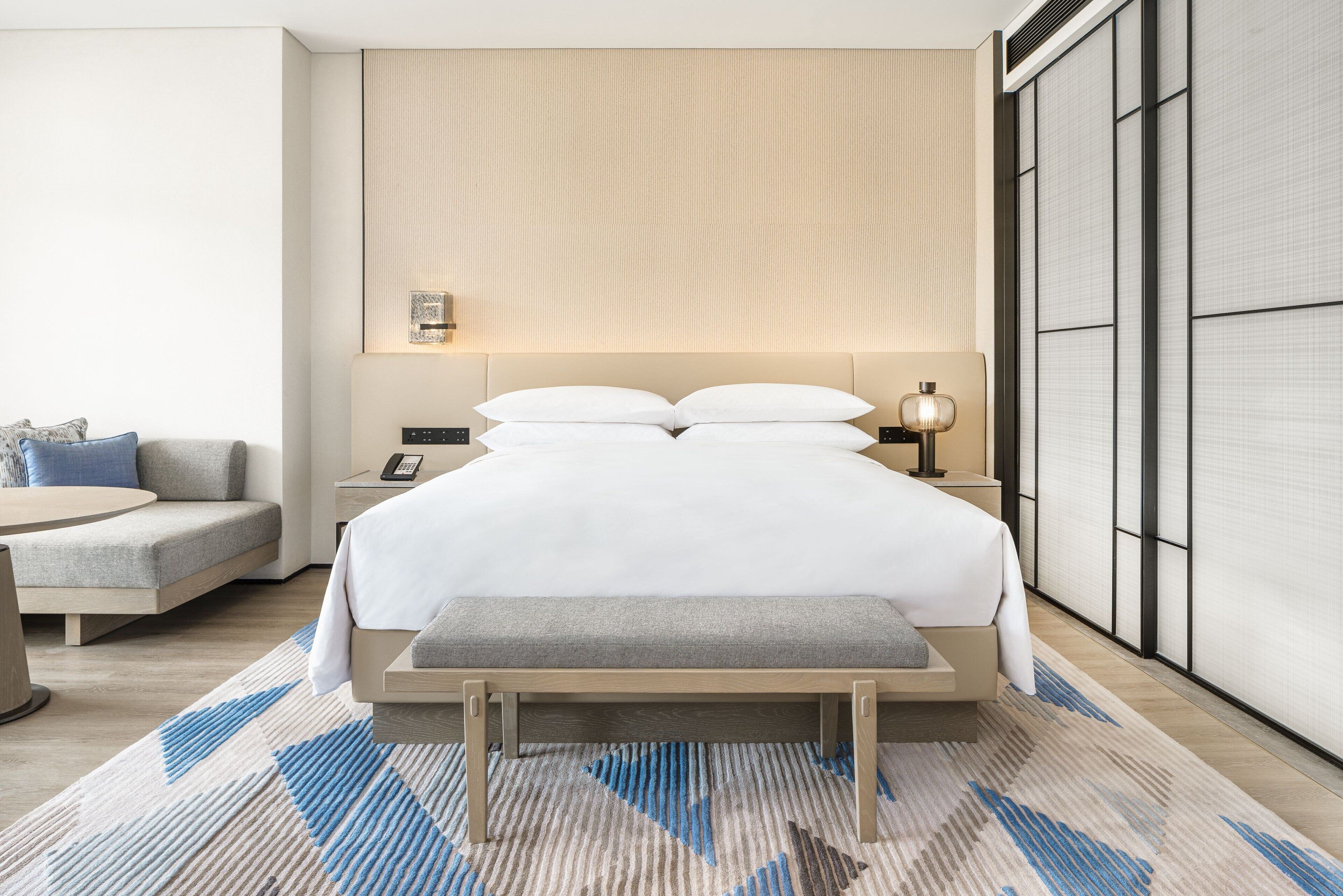 Ein modernes Hotelzimmer mit einem großen Bett, Nachttischen, einer Couch und Blick auf ein traditionelles Gebäude.
