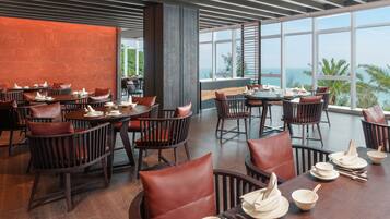 A restaurant with wooden tables and chairs, large windows with a view of the ocean, and a modern interior design.