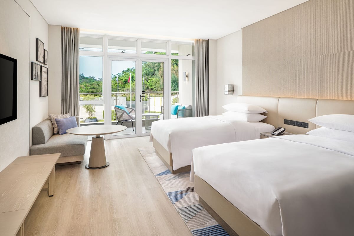 A hotel room with two beds, a sofa, a small table, and a balcony with outdoor furniture.