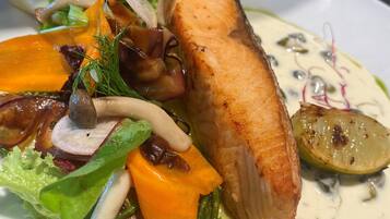 A plate of food with a piece of salmon, vegetables, and a creamy sauce.