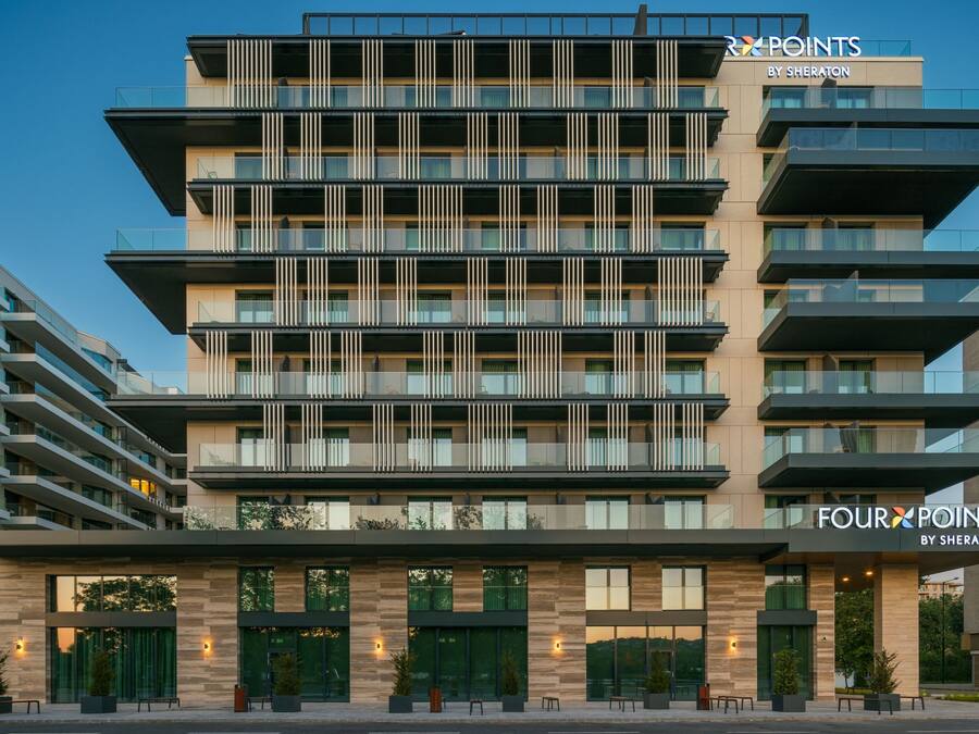 Ein mehrstöckiges Hotel mit modernem Design, das auf jeder Etage Balkone, große Fenster und eine auffällige Beschilderung für "Four Points by Sheraton" bietet.