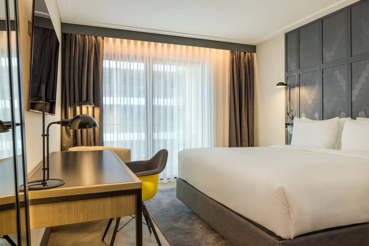 A hotel room with a bed, a desk, a chair, and a large window with curtains.