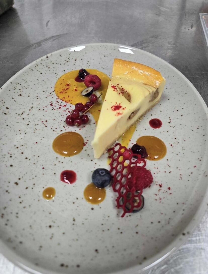 Um prato de sobremesa com uma fatia de cheesecake, frutas vermelhas e calda.
