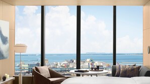 A hotel room with a large window offering a city view, a bed, a round table, and a chair.