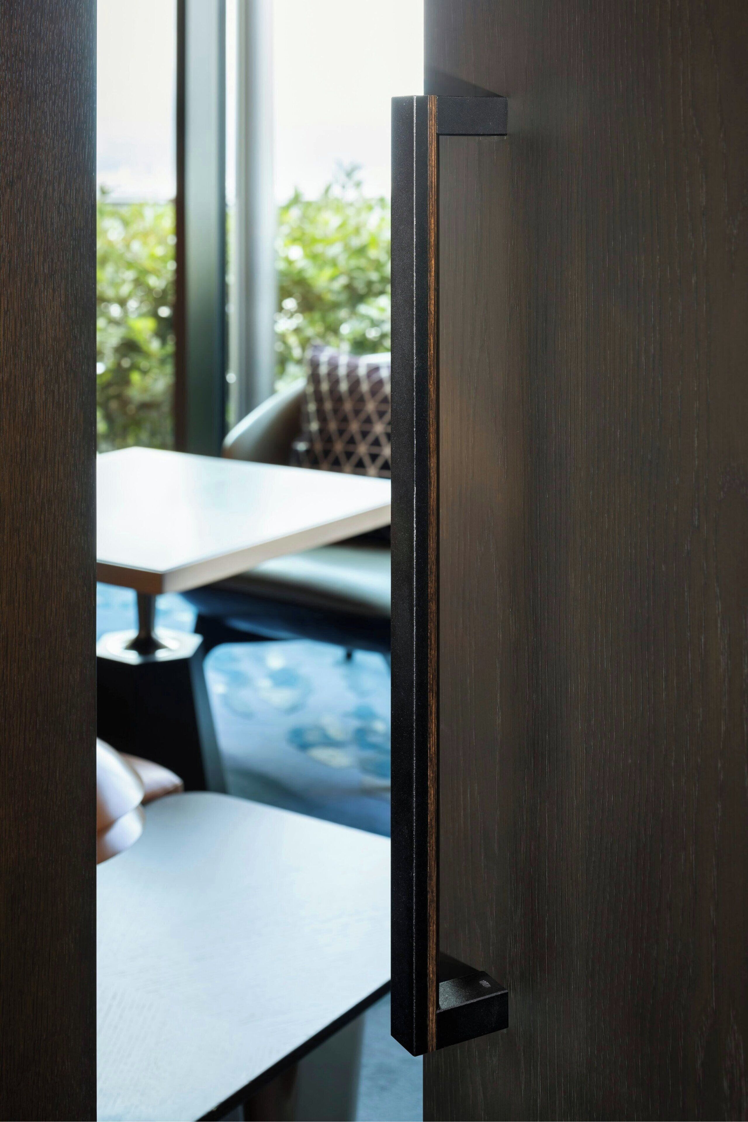 A door with a black handle and a view of an indoor seating area with a table and chairs.