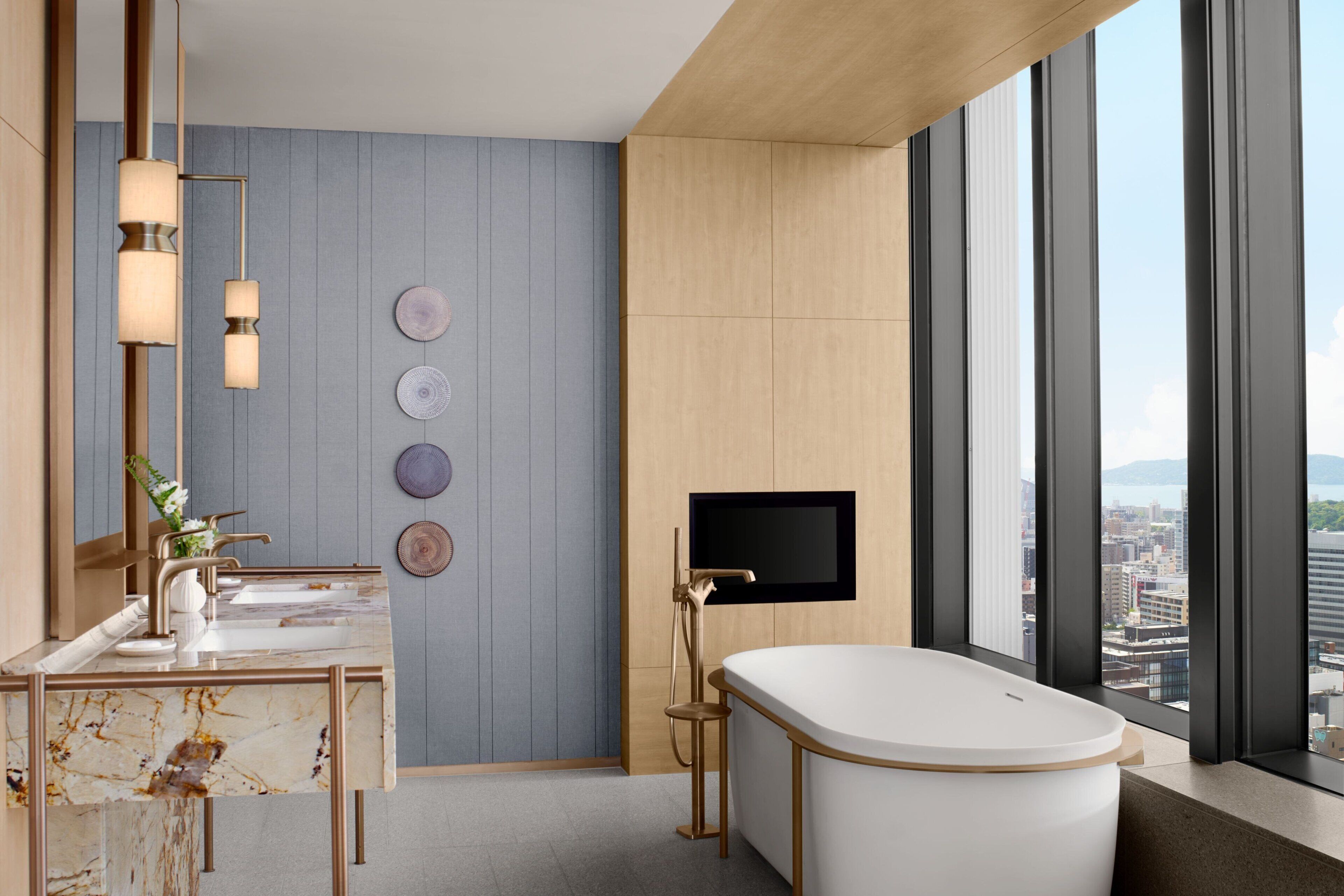 A modern bathroom with a large bathtub, a vanity with a marble countertop, and a wall-mounted TV.