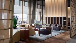 A modern hotel lobby with large windows, a seating area with sofas and chairs, and a decorative wall with vertical panels.