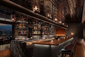 Un bar modern amb un sostre alt, conductes descobertes i vista a la ciutat.