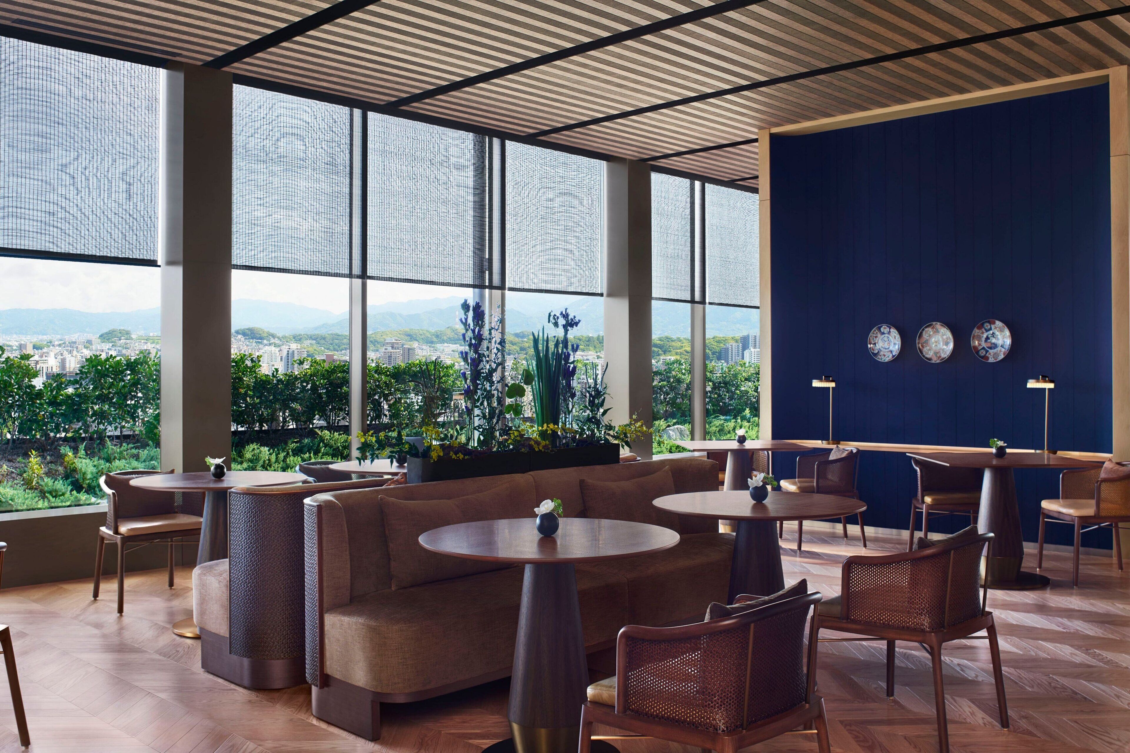 A modern lounge area with round tables and sofas, large windows offering a city view, and decorative plates on the wall.