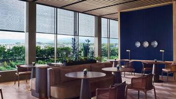 A modern lounge area with round tables and sofas, large windows offering a city view, and decorative plates on the wall.