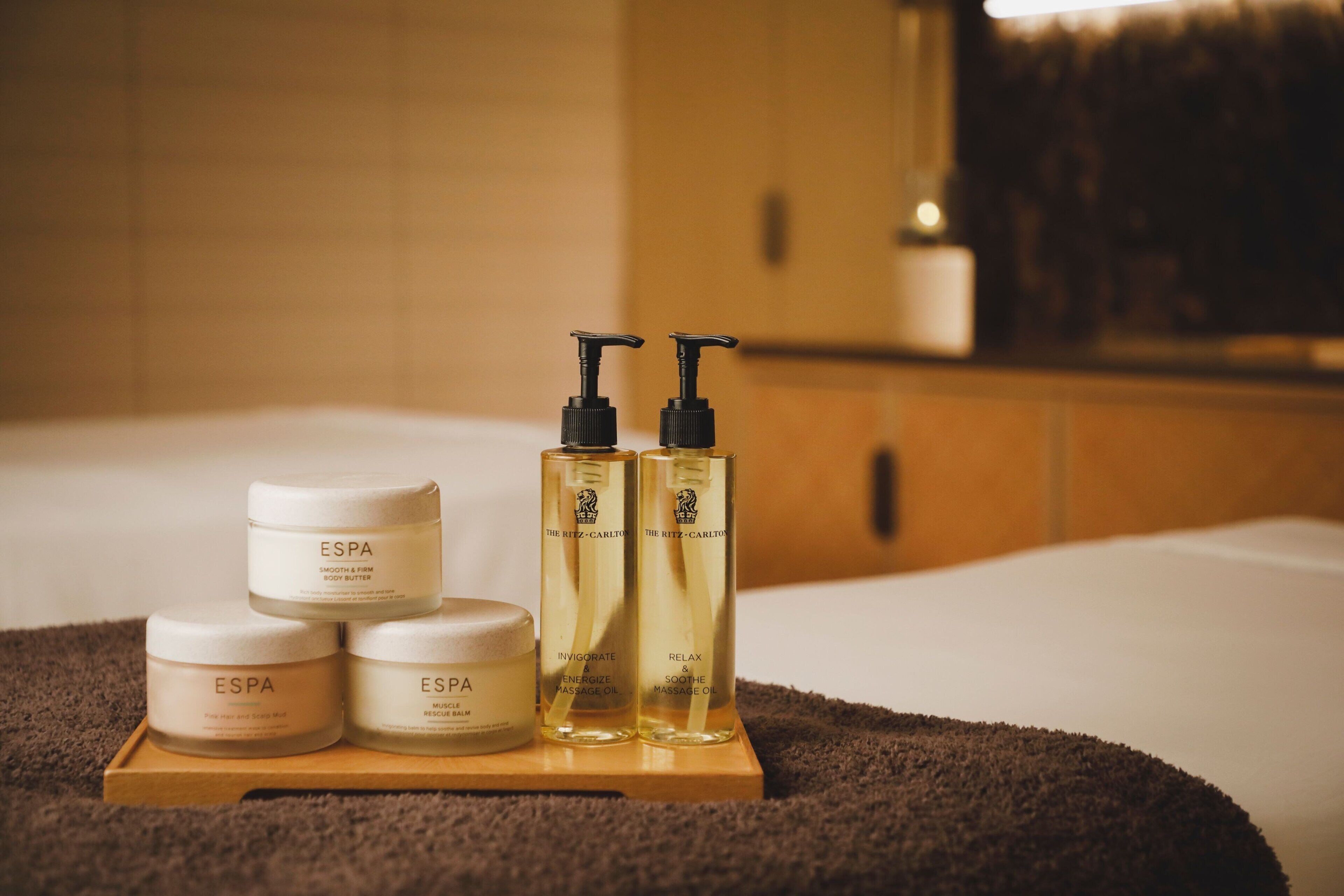 A wooden tray with four jars and two bottles of massage oil on a bed.