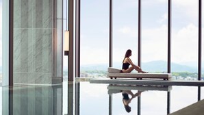 A woman sitting on a bench by a reflective pool with a cityscape view.