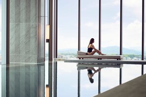 A woman sitting on a bench by a reflective pool with a cityscape view. - The Ritz-Carlton, Fukuoka (Fukuoka)