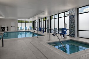 Una piscina interior moderna con agua cristalina, rodeada de amplios ventanales y sillas azules.
