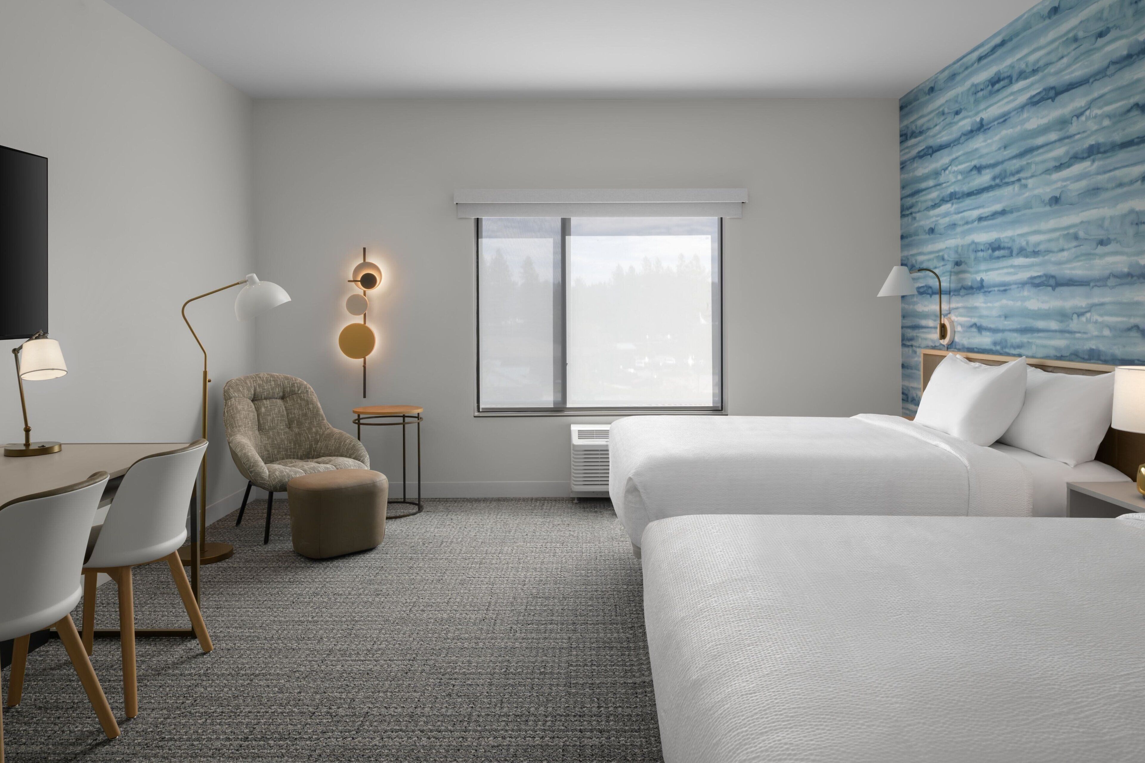 A hotel room with a bed, a desk, a chair, a TV, and a window with a view.