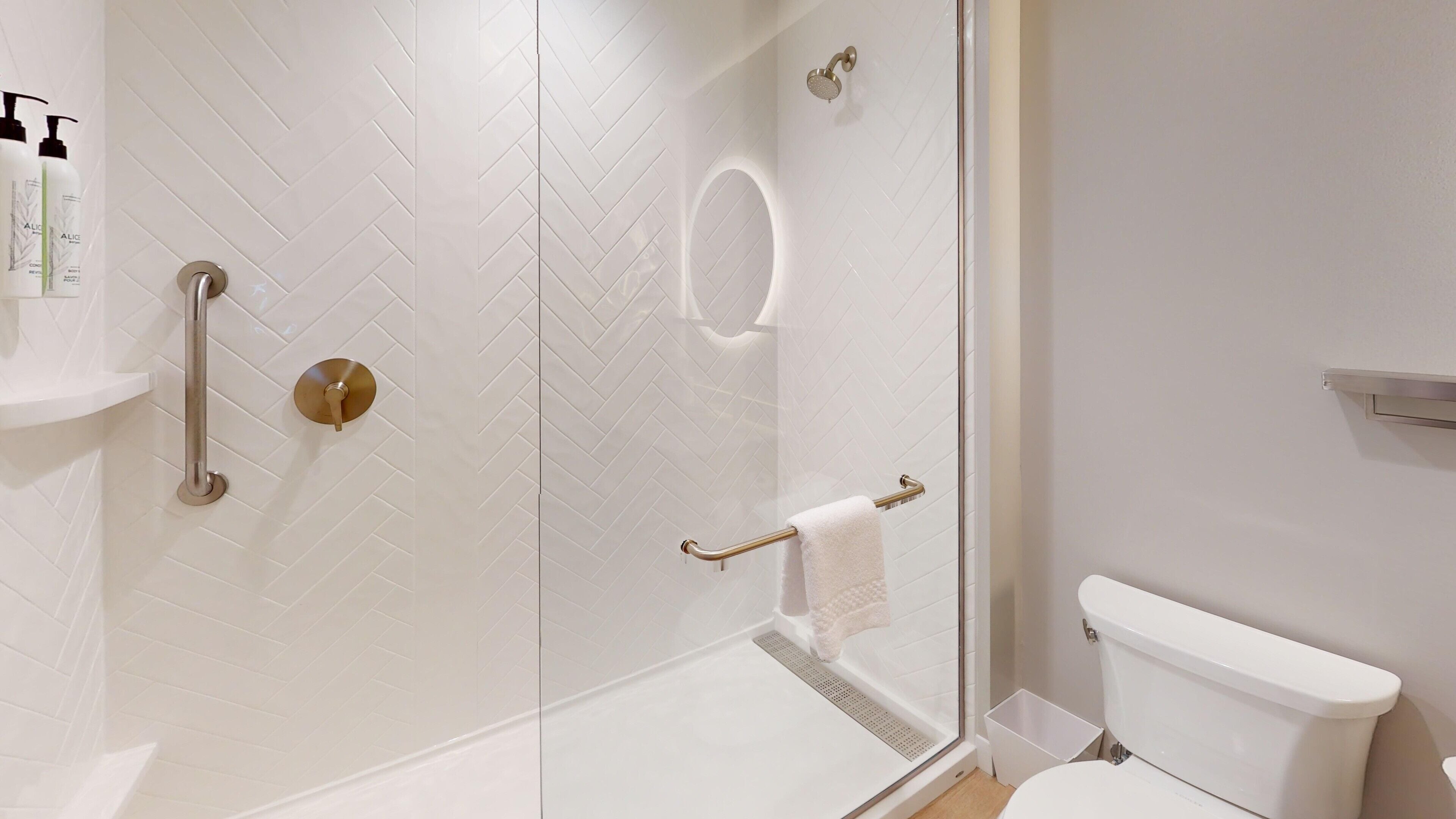 A modern bathroom with a glass shower enclosure, a toilet, and a handrail.