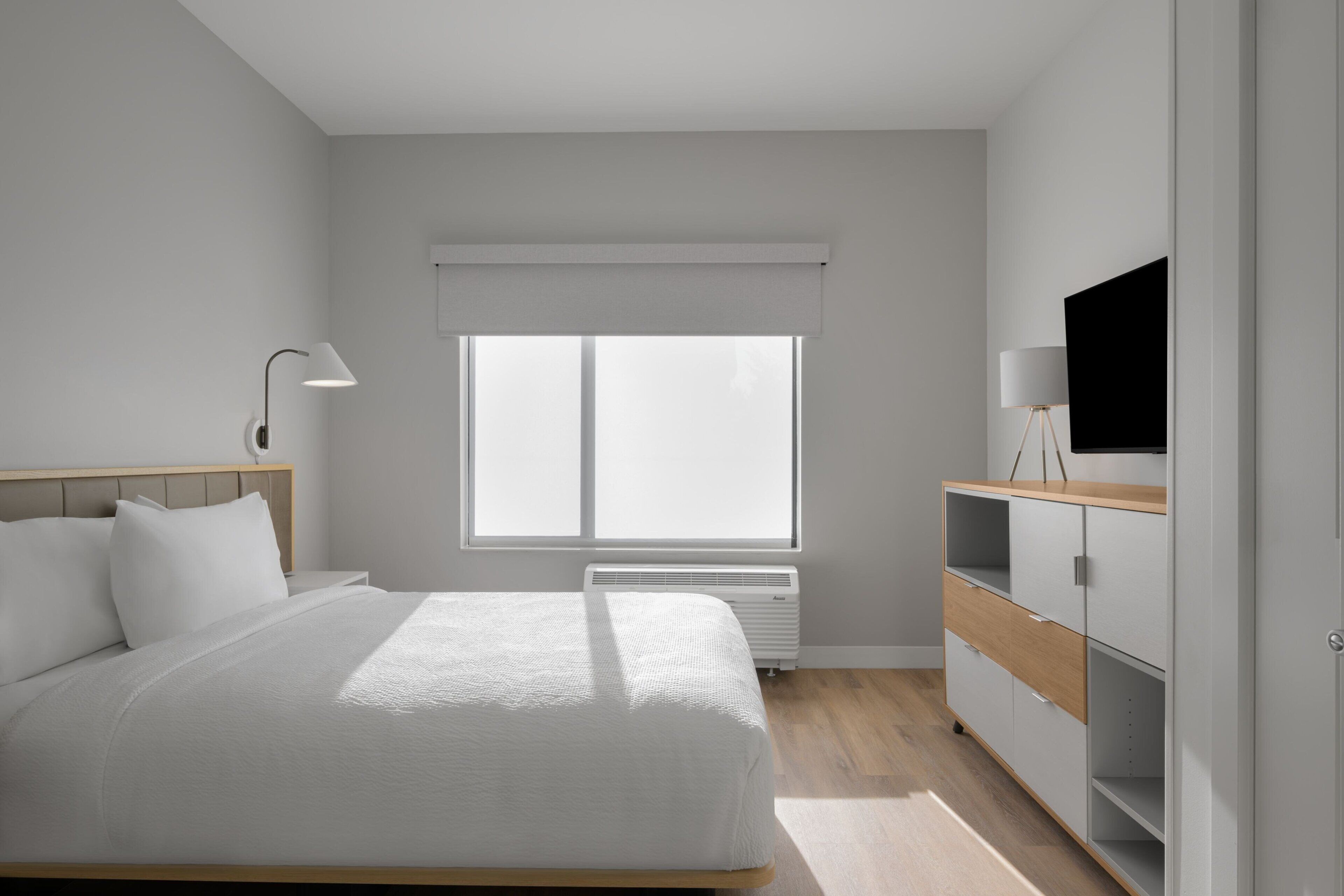 A modern bedroom with a bed, bedside lamp, TV, and built-in shelving.