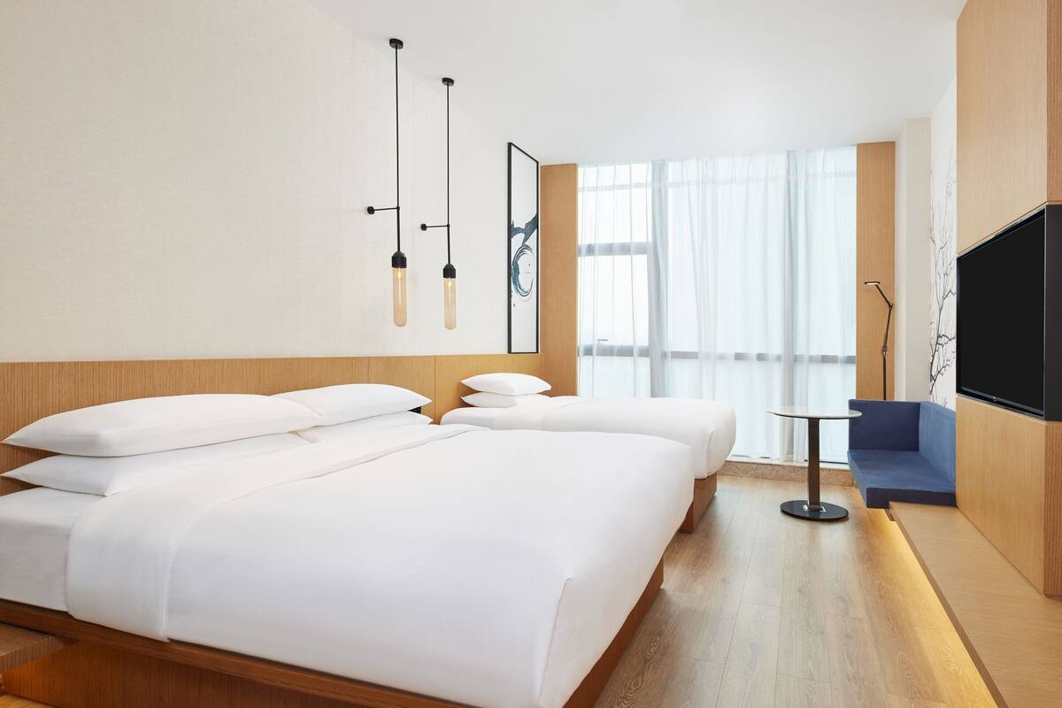 A modern hotel room with a large bed, a small sofa, a TV, and a window with sheer curtains.