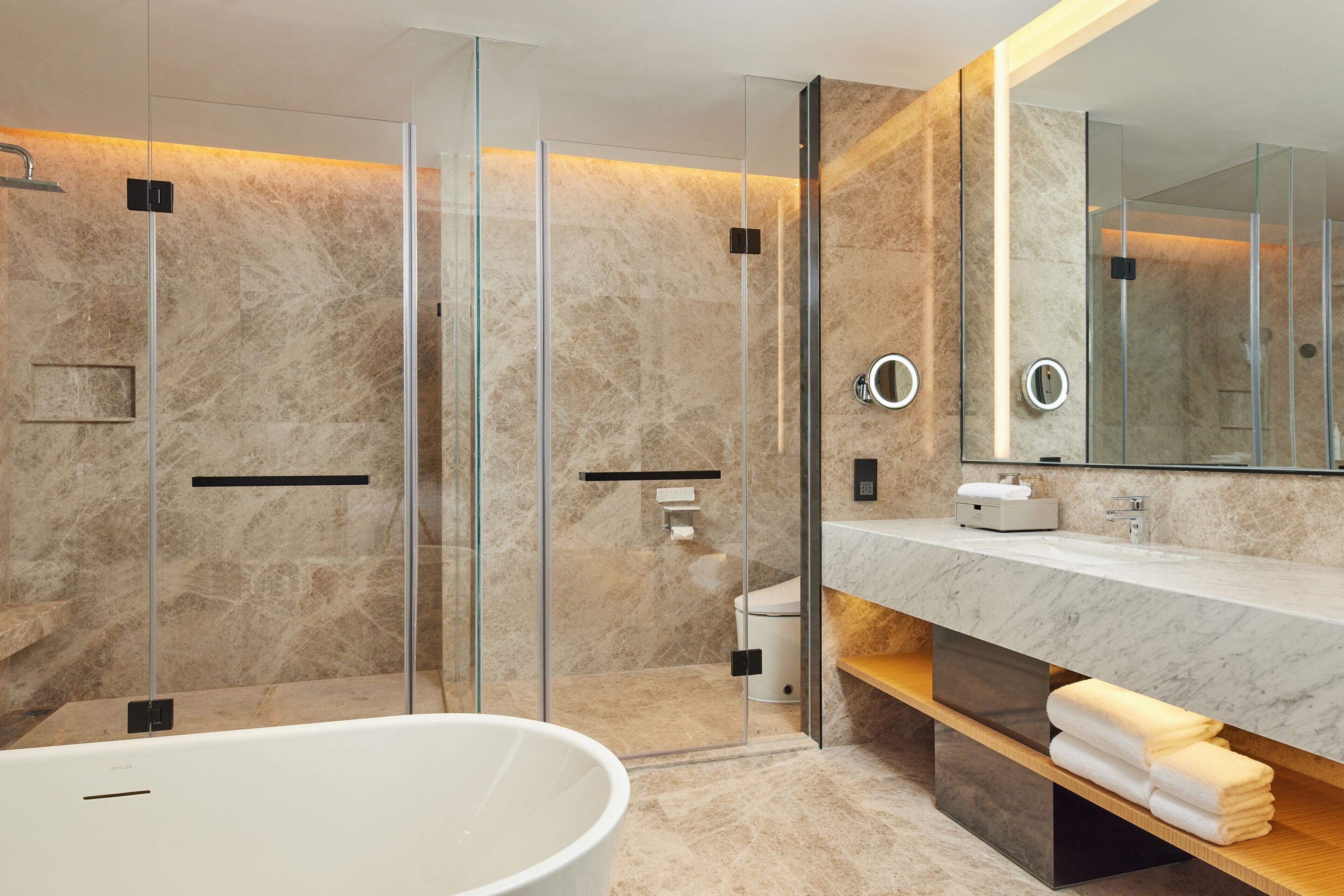 Een moderne badkamer met een douchecabine van glas, een ruime badkuip en een marmeren aanrechtblad.