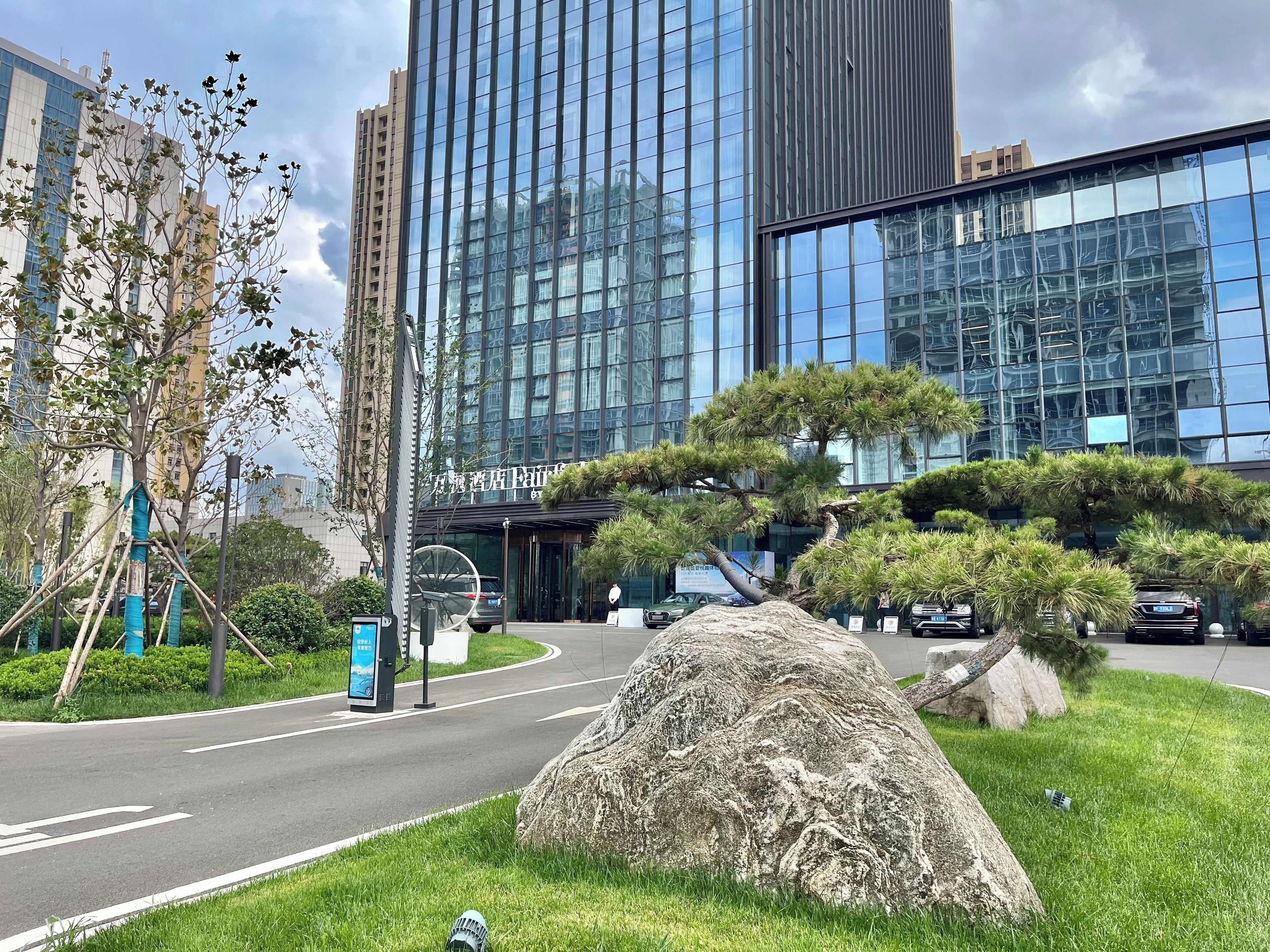 Un edificio moderno con fachada de vidrio, una gran roca ornamental y un césped bien cuidado.