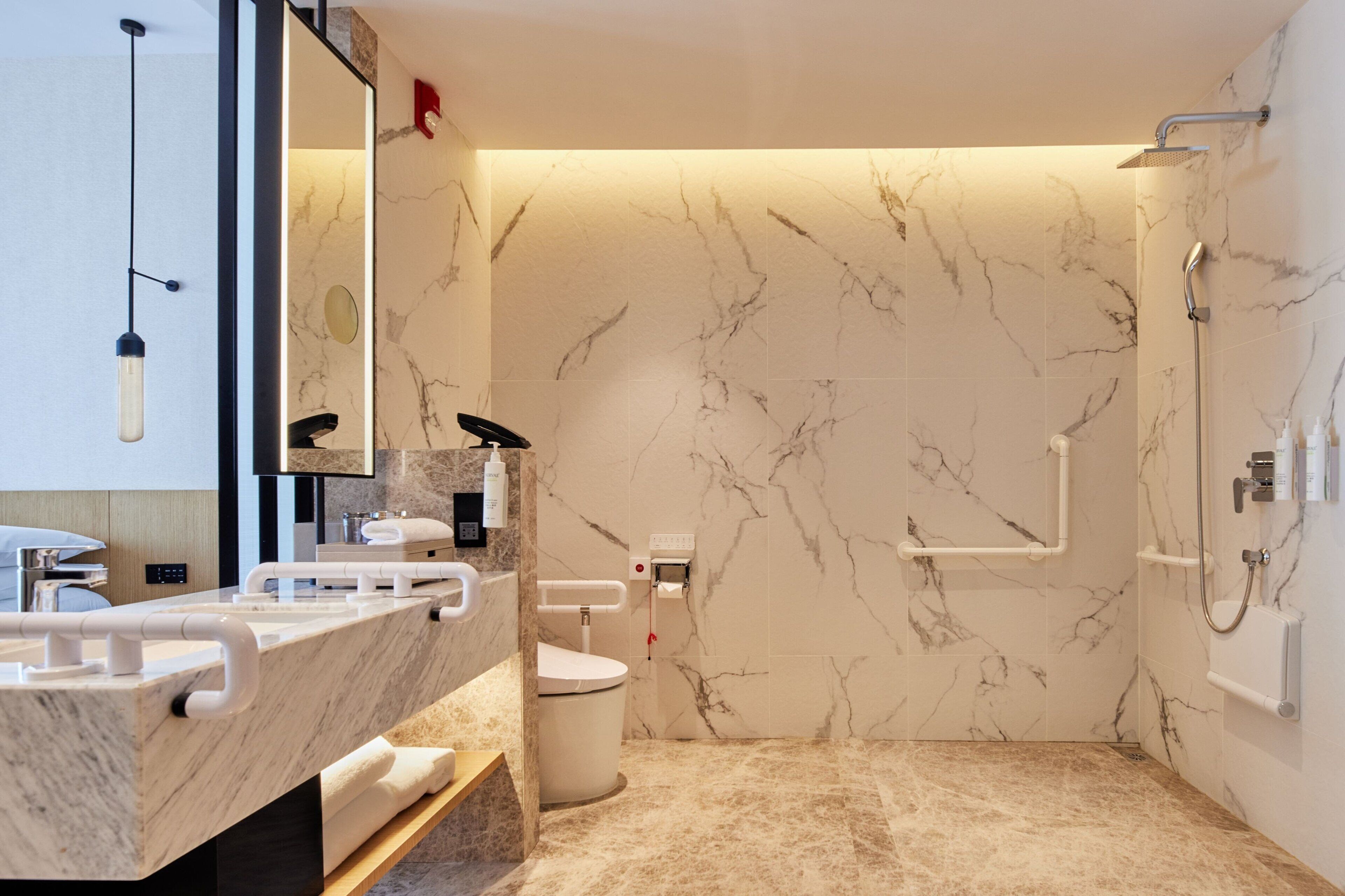 Een moderne badkamer met een marmeren wand, een douche en een wastafel met spiegel.