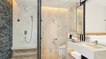 Un baño moderno con ducha de vidrio, pared de azulejos de mármol, espejo grande y lavamanos blanco.