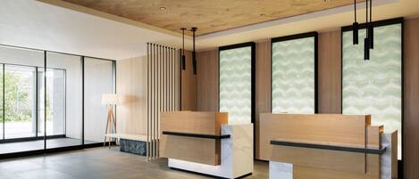 A modern reception area with wooden reception desks, a standing lamp, and large windows with patterned glass.