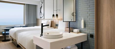 Habitación de hotel moderna con una cama grande, un lavabo redondo, un espejo y vista al mar.