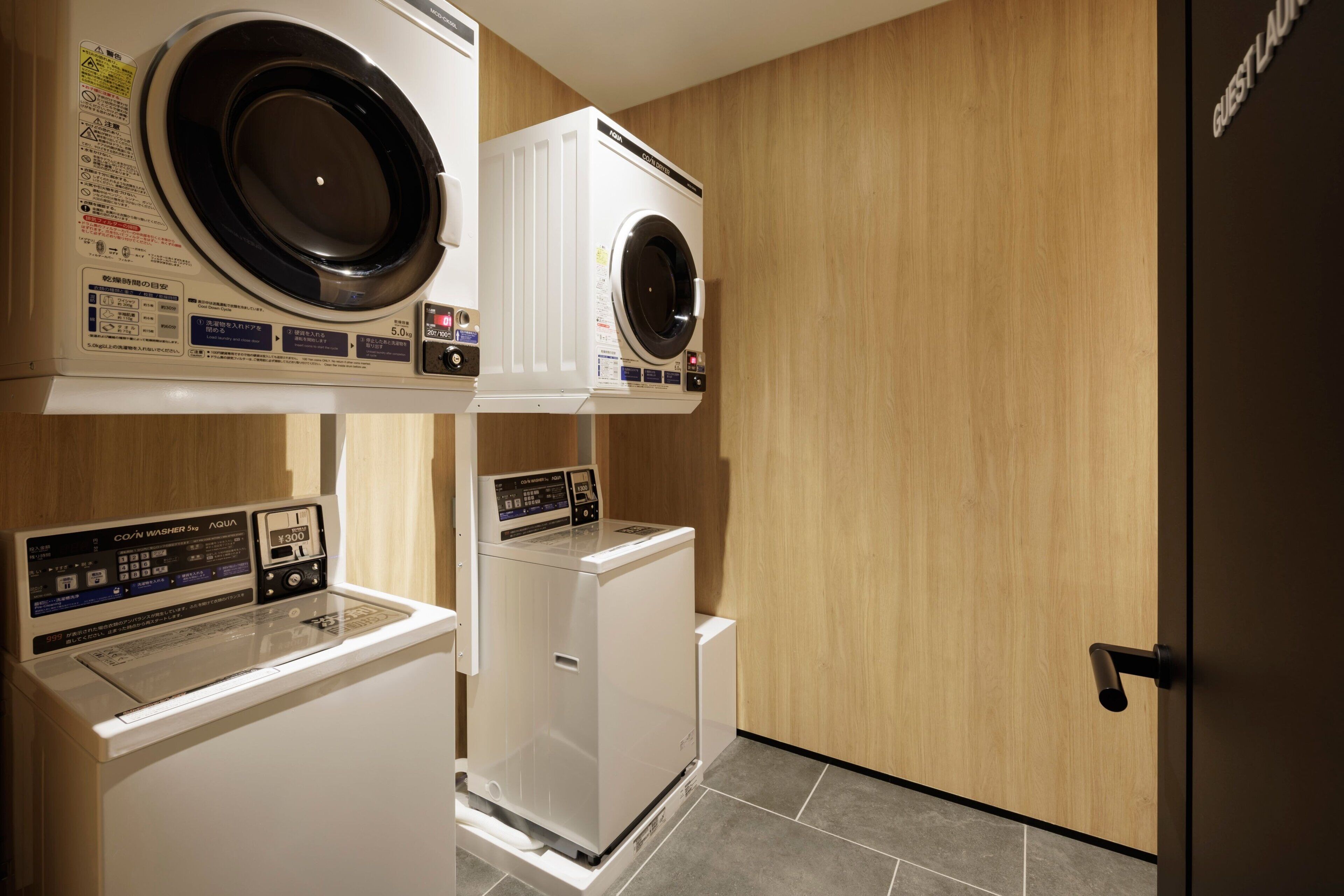 A laundry room with two front-loading washing machines and a dryer, wooden walls, and a door with a sign.