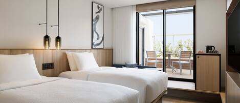 A hotel room with two beds, a balcony with a table and chairs, a TV, and a coffee maker.