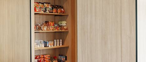 A wooden pantry with shelves stocked with various food items, including snacks, beverages, and packaged goods.