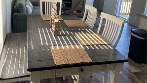 Un coin repas avec une table et des chaises en bois, un téléviseur et un canapé à l’arrière-plan.