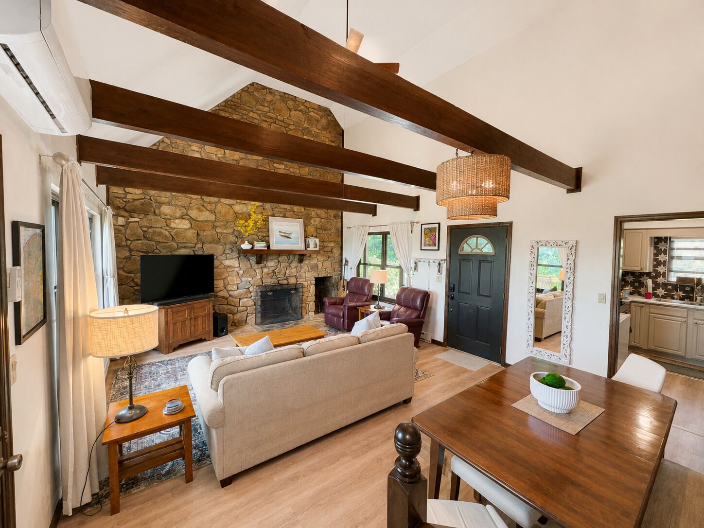 Een ruime woonkamer met een stenen openhaard, een televisie, leren fauteuils en een eettafel met een schaal groen.