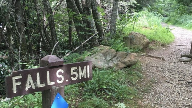 Ein hölzernes Wegweiser mit der Aufschrift 'FALLS. 5MI', der eine Entfernung anzeigt.