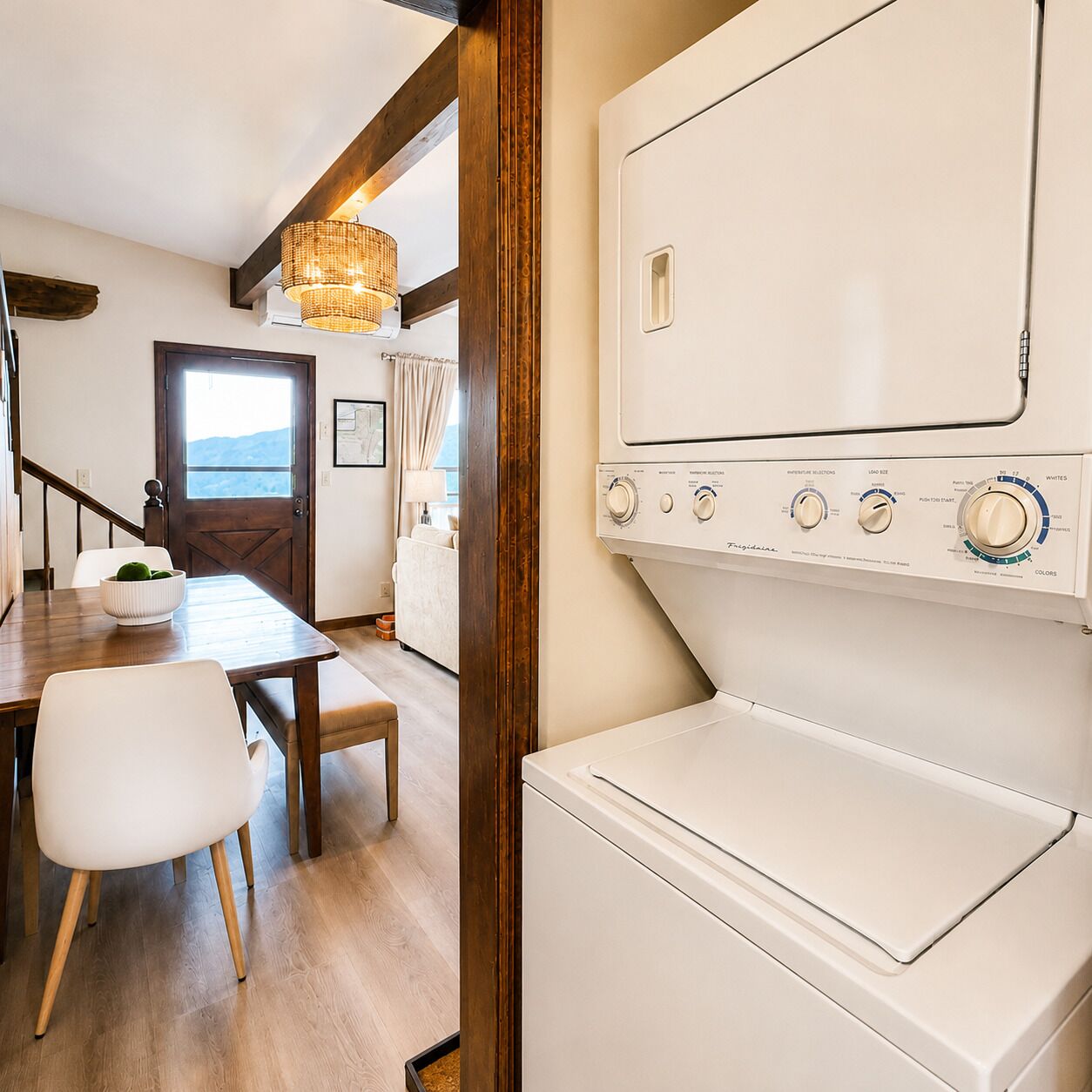 Een wasserette met een witte wasmachine, houten vloeren en een eethoek met tafel en stoelen.