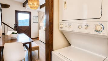 Een wasserette met een witte wasmachine, houten vloeren en een eethoek met tafel en stoelen.