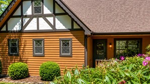 A traditional half-timbered house with a sloped roof and a well-maintained garden with various plants and flowers.