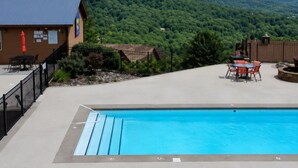 A pool area with a view of mountains, a covered seating area, and a building with a flag.